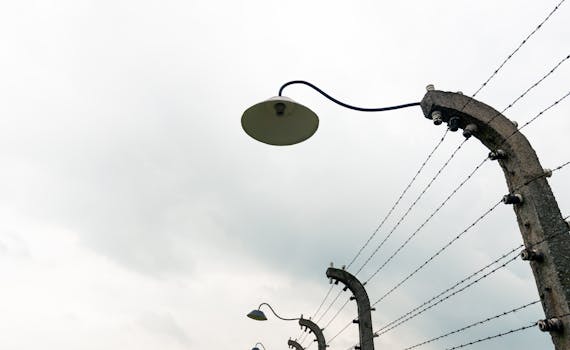 pexels photo 13603330 13603330 Low angle view of an overcast sky with barbed wire fence and lamps.
